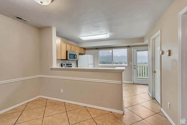 kitchen featuring freestanding refrigerator, stainless steel microwave, light tile patterned flooring, a peninsula, and a textured ceiling