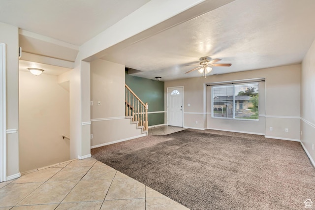 tiled entrance foyer featuring stairs, a ceiling fan, carpet flooring, and baseboards