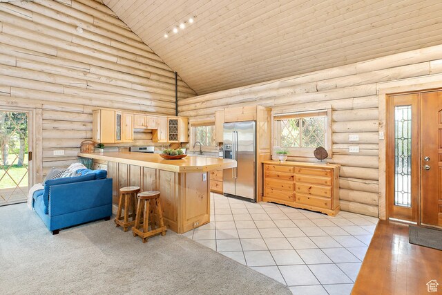kitchen with stainless steel appliances, high vaulted ceiling, a peninsula, rustic walls, and light brown cabinetry