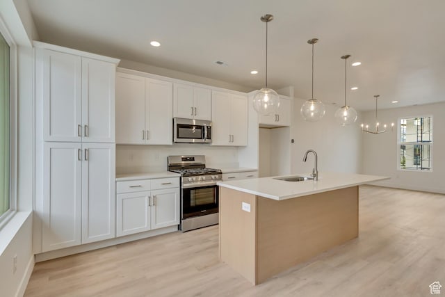 kitchen featuring appliances with stainless steel finishes, a sink, light wood-style flooring, white cabinets, and a center island with sink