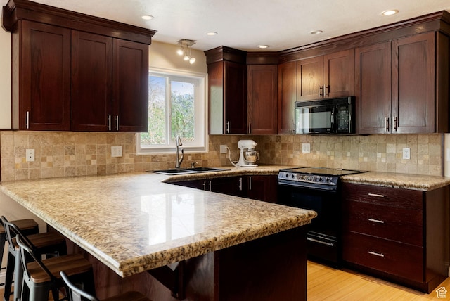 kitchen featuring black appliances, a sink, a peninsula, a breakfast bar area, and light wood-type flooring