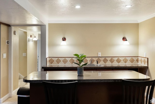 kitchen with a sink, dark countertops, a kitchen breakfast bar, and ornamental molding