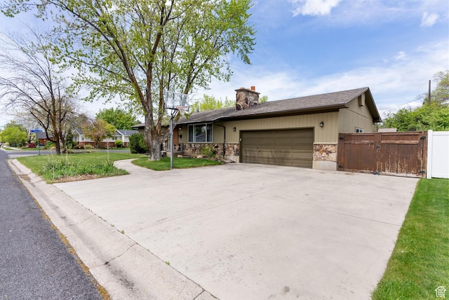 ranch-style home featuring stone siding, an attached garage, concrete driveway, a gate, and a chimney