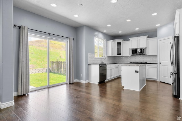 kitchen with stainless steel appliances, a sink, a center island, tasteful backsplash, and baseboards