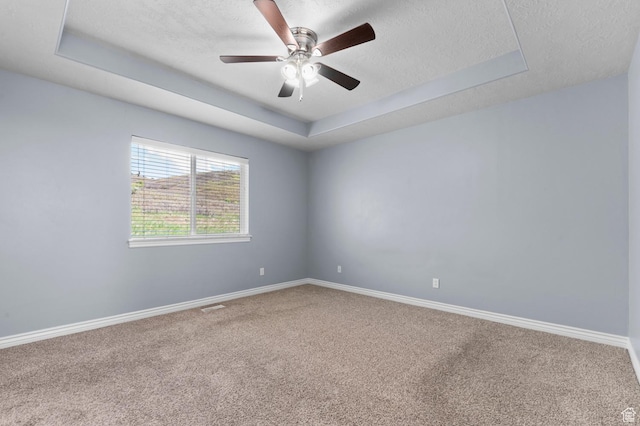 spare room featuring a raised ceiling, carpet flooring, a textured ceiling, a ceiling fan, and baseboards