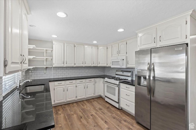 kitchen featuring white appliances, dark countertops, open shelves, white cabinetry, and recessed lighting
