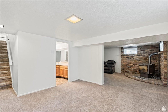 below grade area with light colored carpet, a wood stove, stairway, baseboards, and a textured ceiling