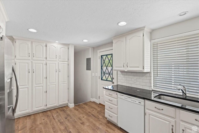 kitchen with white dishwasher, a sink, dark countertops, light wood-style flooring, and white cabinets