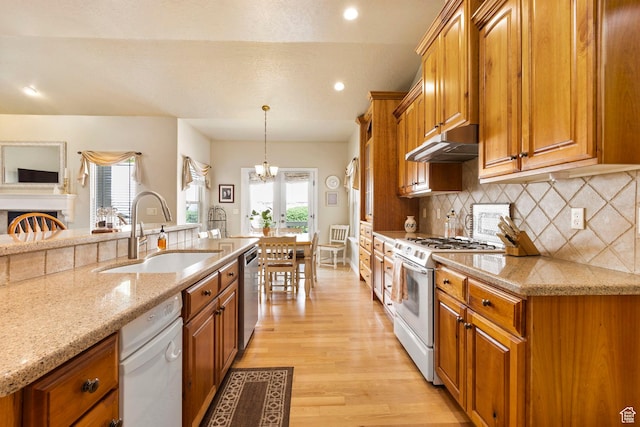 kitchen featuring white gas range oven, a sink, under cabinet range hood, dishwasher, and brown cabinetry