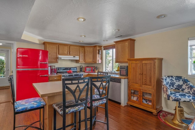 kitchen with appliances with stainless steel finishes, under cabinet range hood, wood finished floors, brown cabinets, and ornamental molding