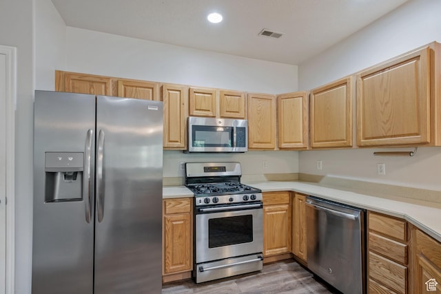 kitchen with appliances with stainless steel finishes, light countertops, wood finished floors, light brown cabinets, and recessed lighting