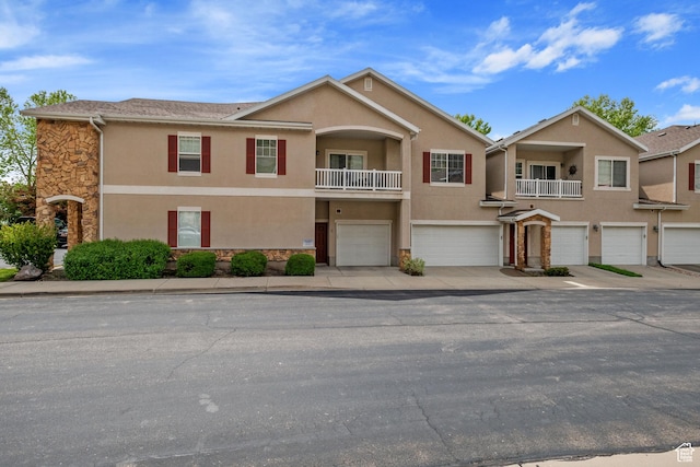 view of property with stone siding, a garage, stucco siding, a balcony, and driveway
