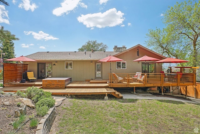 back of house with a deck, a lawn, a chimney, and a shingled roof