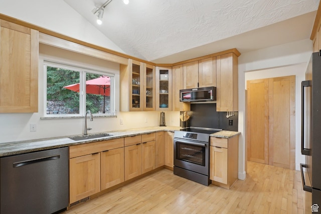 kitchen featuring appliances with stainless steel finishes, a sink, light brown cabinets, light wood-style floors, and light stone counters