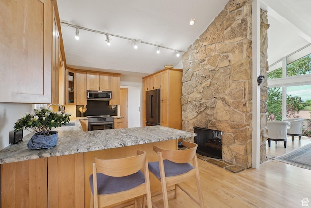 kitchen with stainless steel microwave, stove, high end black refrigerator, light brown cabinets, and light wood-style floors
