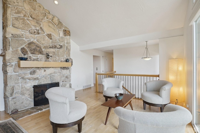 sitting room featuring wood finished floors, lofted ceiling, and a stone fireplace