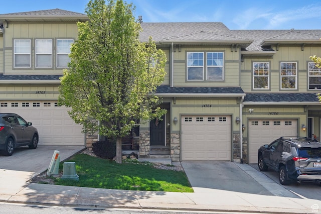 townhome / multi-family property with driveway, an attached garage, board and batten siding, stone siding, and a shingled roof