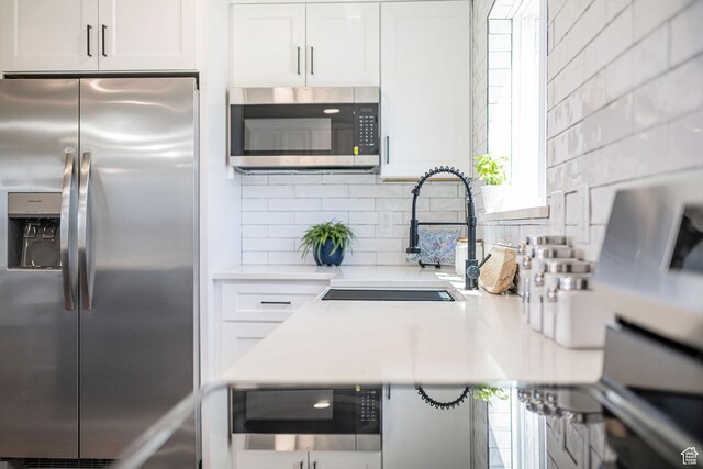kitchen with stainless steel appliances, light countertops, a sink, white cabinetry, and backsplash