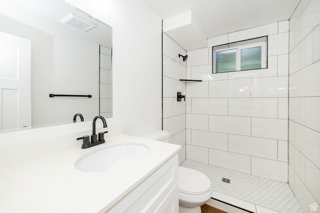 bathroom featuring toilet, tiled shower, and vanity