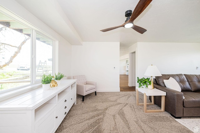 living area with light colored carpet, a ceiling fan, and baseboards