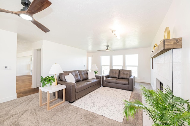 carpeted living area with ceiling fan, a tiled fireplace, and baseboards