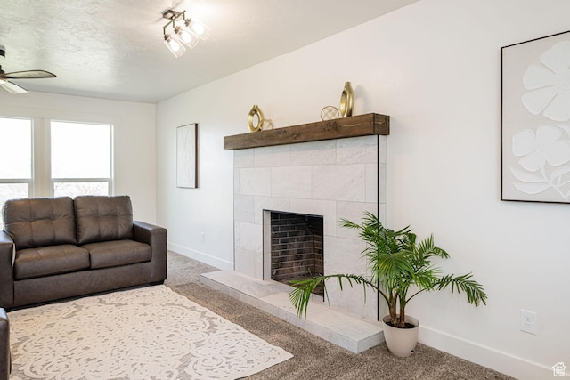 carpeted living area featuring baseboards, ceiling fan, a fireplace, and a textured ceiling