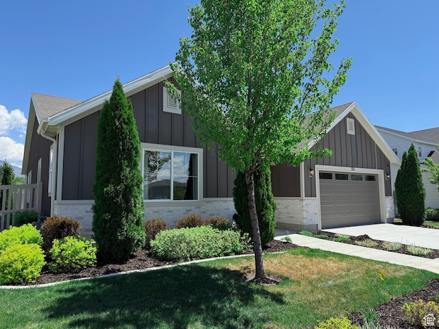 view of front of home featuring board and batten siding, a garage, driveway, a front yard, and brick siding