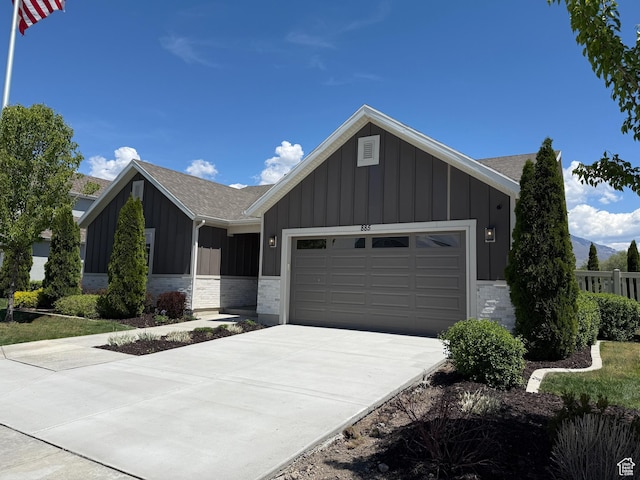 ranch-style house with board and batten siding, an attached garage, concrete driveway, roof with shingles, and stone siding