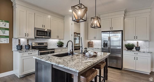 kitchen featuring appliances with stainless steel finishes, a sink, wood finished floors, tasteful backsplash, and light stone countertops