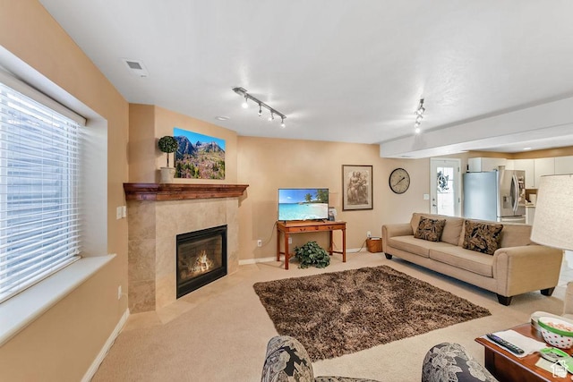 living area featuring light carpet, rail lighting, a tile fireplace, and baseboards