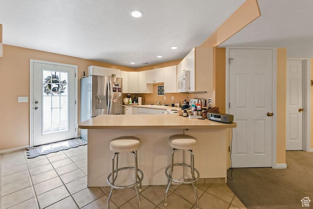 kitchen with stainless steel fridge, a peninsula, white microwave, light countertops, and a kitchen bar