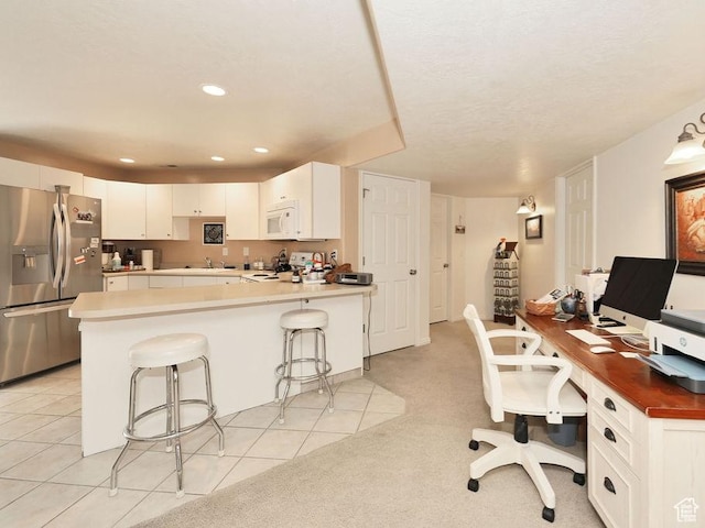 kitchen featuring stainless steel refrigerator with ice dispenser, range, white microwave, an office area, and a breakfast bar area