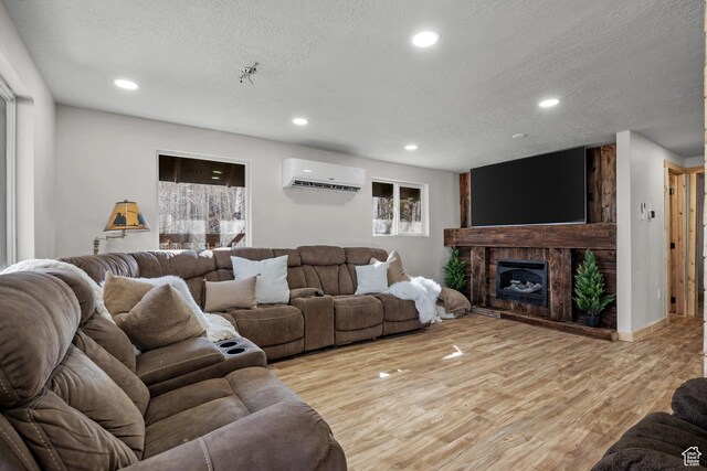 living room featuring a wall mounted air conditioner, a textured ceiling, light wood finished floors, recessed lighting, and a fireplace with raised hearth