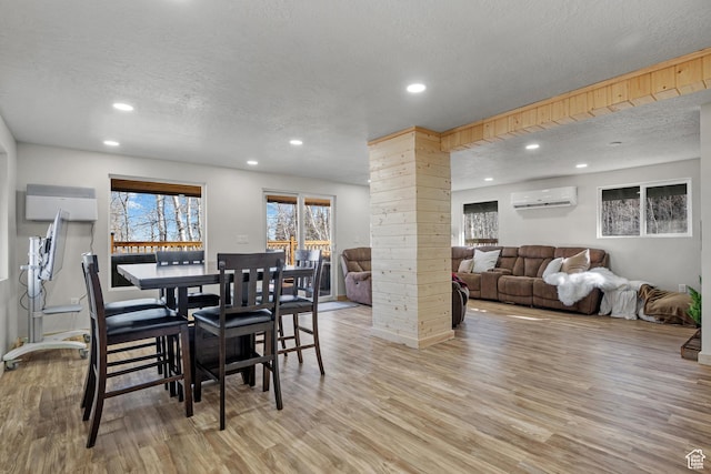 dining area with a textured ceiling, a wall mounted air conditioner, recessed lighting, light wood-style flooring, and ornate columns