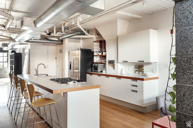 kitchen with a sink, appliances with stainless steel finishes, white cabinetry, a kitchen bar, and modern cabinets