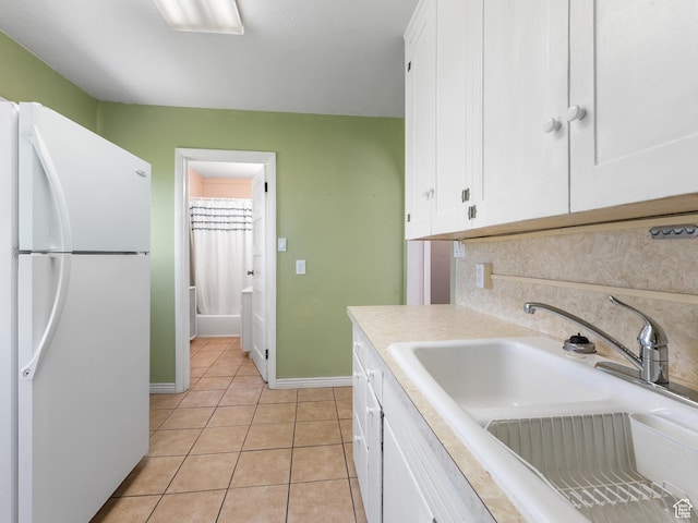 kitchen with freestanding refrigerator, a sink, white cabinetry, light countertops, and light tile patterned flooring