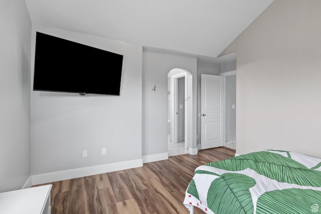 bedroom with arched walkways, wood finished floors, baseboards, and lofted ceiling
