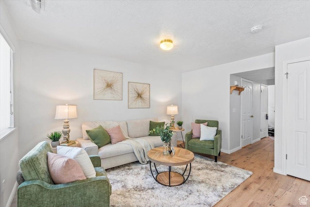 living area featuring light wood-type flooring, baseboards, and a textured ceiling
