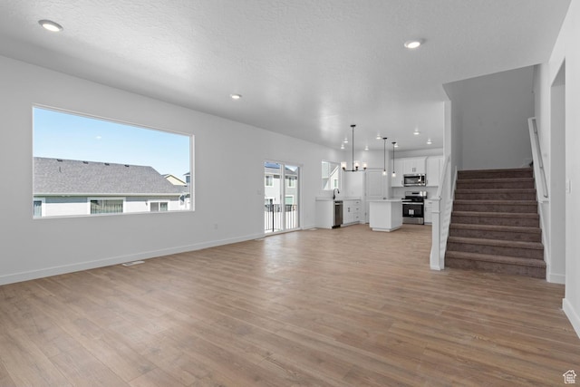unfurnished living room featuring light wood-style flooring, stairway, recessed lighting, and baseboards