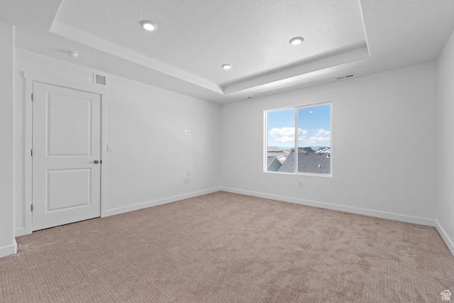 spare room featuring a tray ceiling, light carpet, baseboards, and recessed lighting