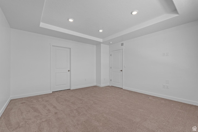 spare room with a raised ceiling, recessed lighting, light colored carpet, and baseboards