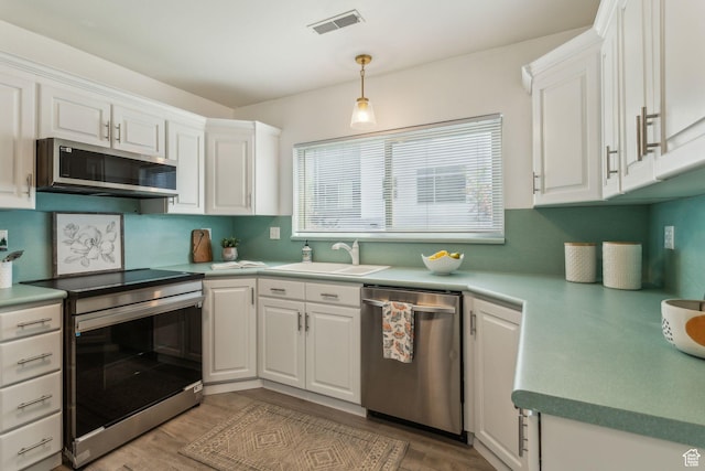 kitchen with appliances with stainless steel finishes, a sink, white cabinets, and light wood-type flooring