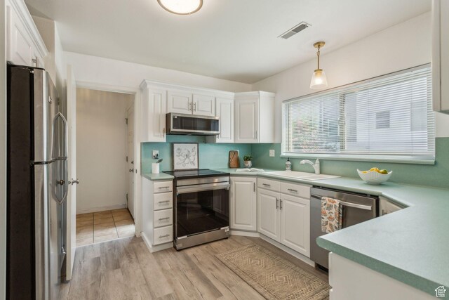 kitchen with stainless steel appliances, a sink, white cabinetry, and light countertops