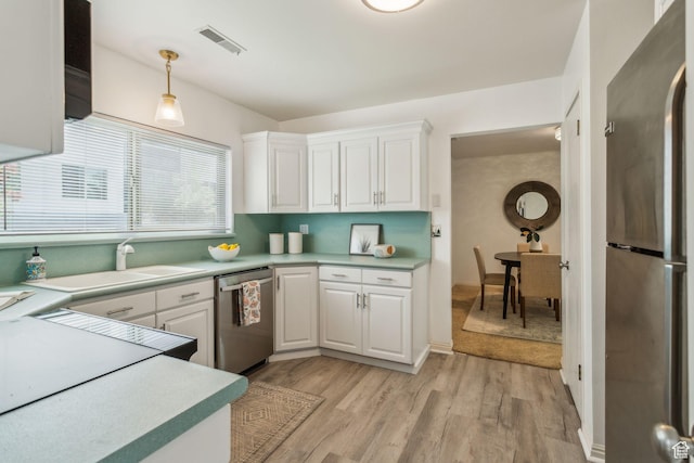 kitchen with stainless steel appliances, light countertops, white cabinets, light wood-type flooring, and a sink