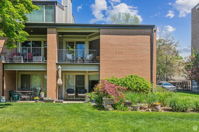 back of house featuring a balcony, brick siding, and a lawn