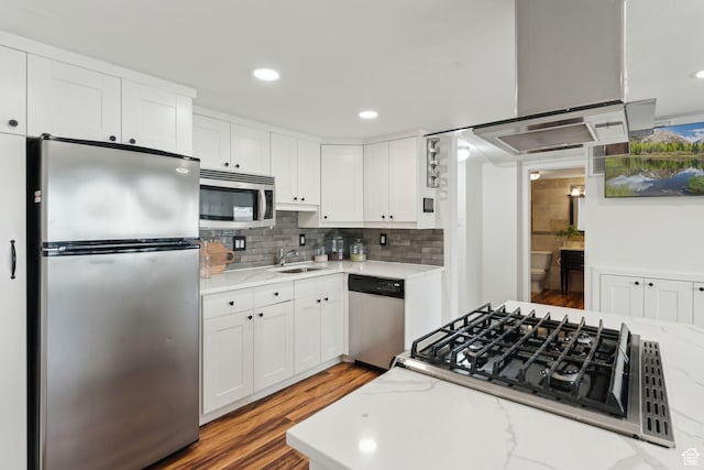 kitchen with appliances with stainless steel finishes, white cabinets, light wood-style floors, backsplash, and a sink