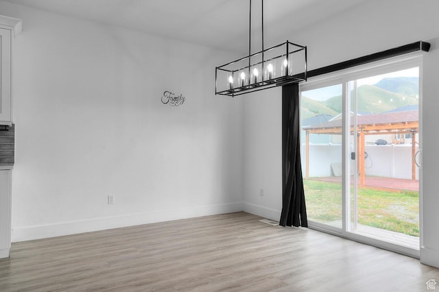 unfurnished dining area featuring light wood finished floors, a chandelier, and baseboards