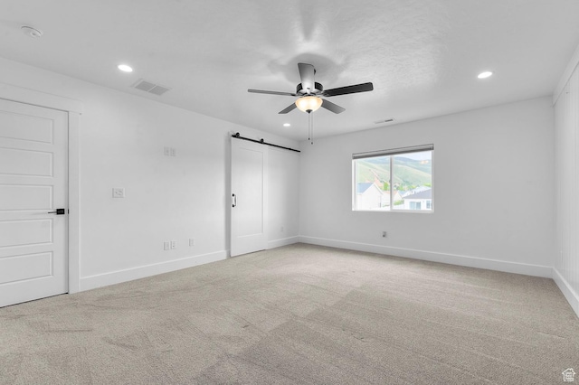 spare room with a barn door, light carpet, a ceiling fan, and recessed lighting