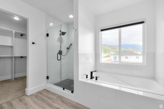 full bathroom featuring a shower stall, wood finished floors, a bath, a walk in closet, and recessed lighting