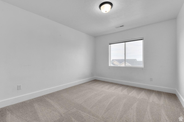 spare room featuring light colored carpet and baseboards
